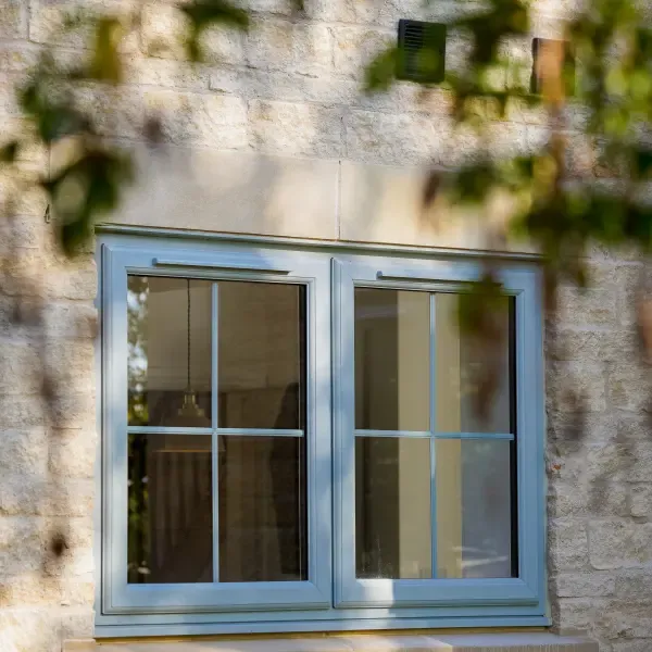 Grey casement window with glazing bars set in a stone wall