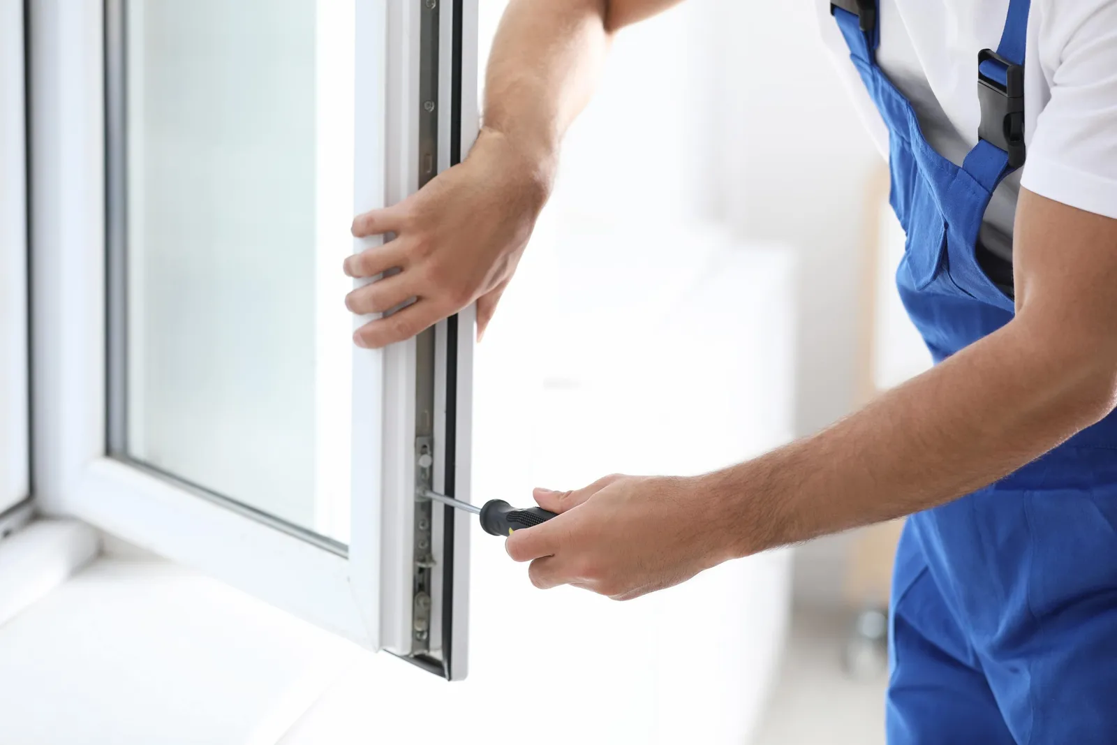Person in blue overalls working on an open white window